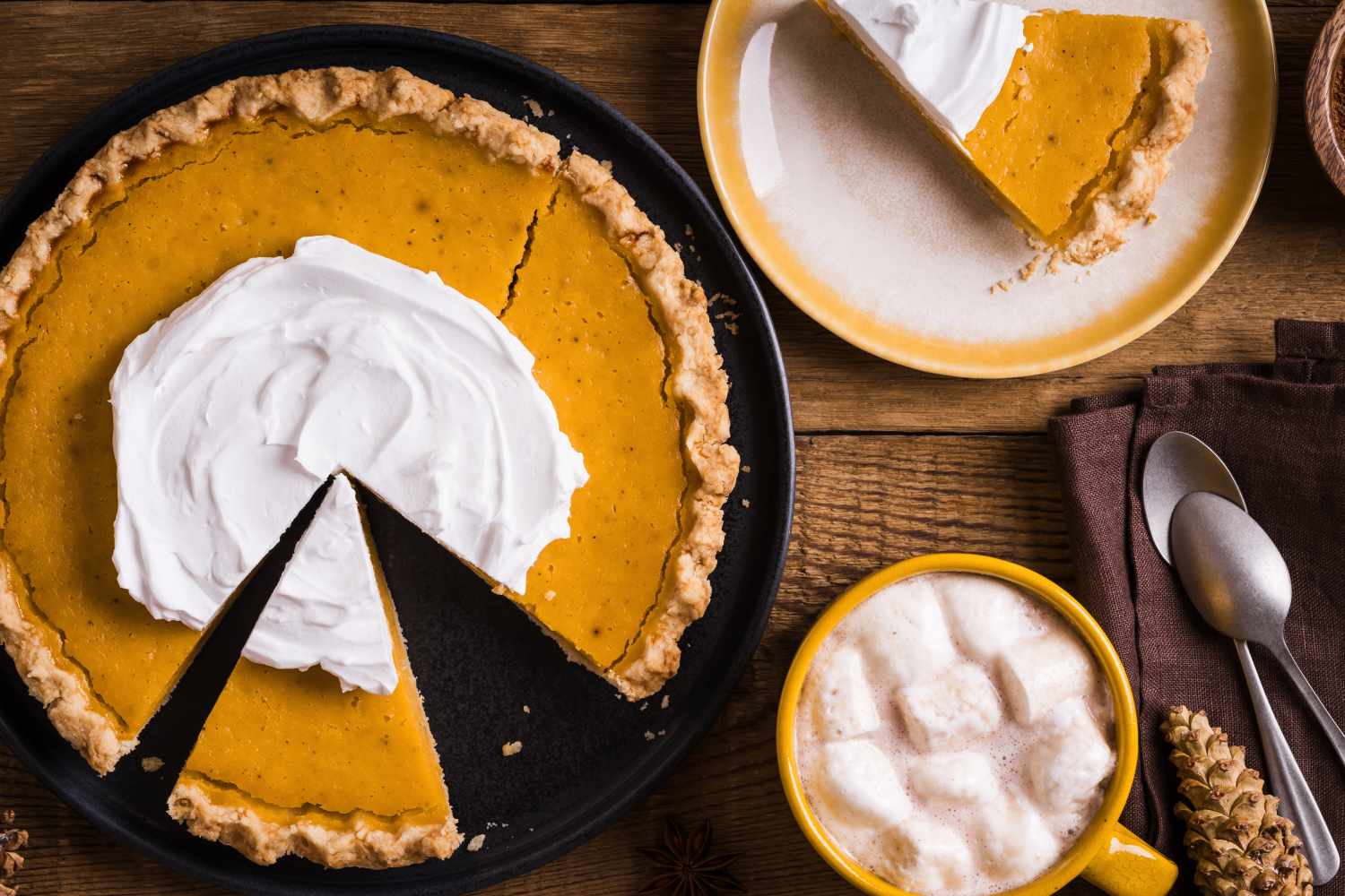 Pumpkin pie with whipped cream a coffee cup and utensils on a wooden table