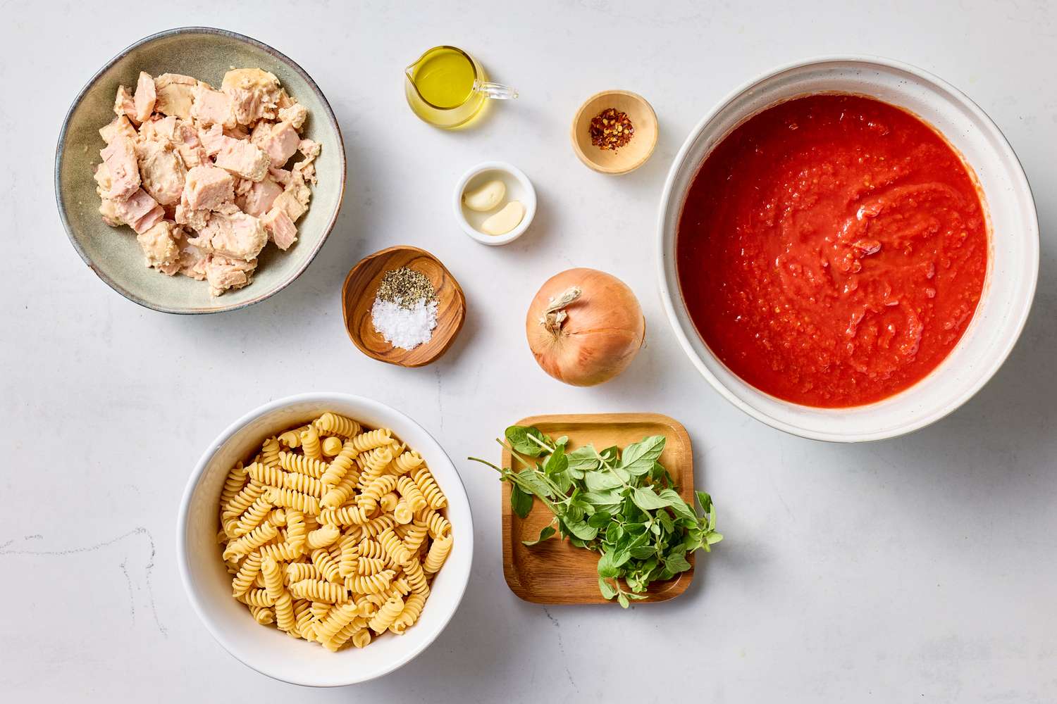 Ingredients for a tuna and tomato pasta dish displayed including tuna pasta tomato sauce onion arugula spices and oil