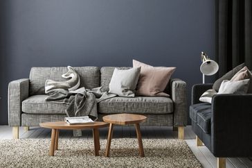 A modern living room with a sofa throw blankets cushions two wooden coffee tables and a floor lamp