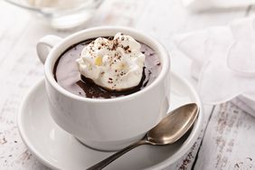 A cup of hot chocolate topped with whipped cream on a saucer with a spoon beside it