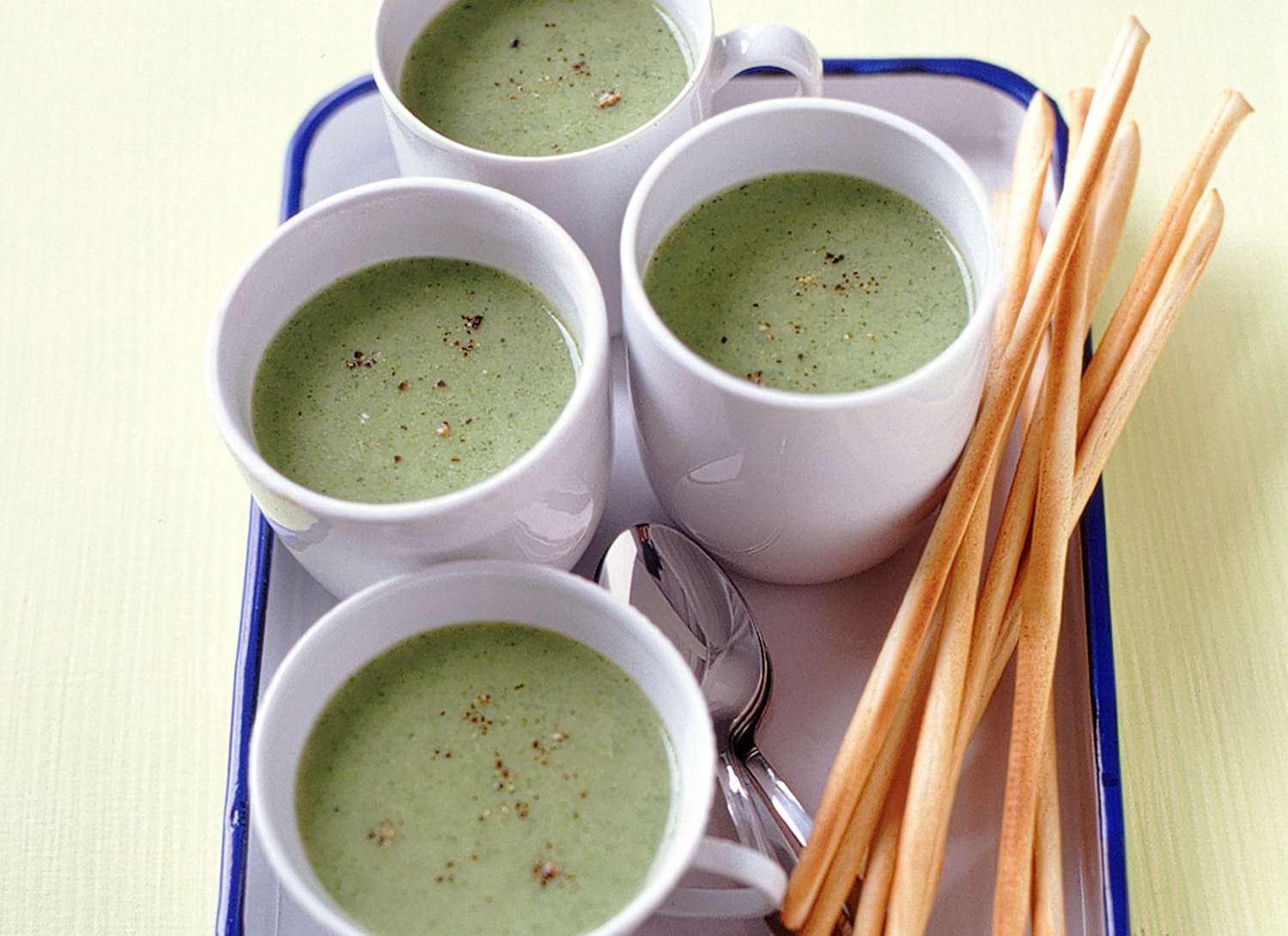 multiple mugs of creamy broccoli soup on a white tray