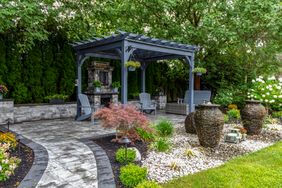 Outdoor seating area with a pergola, surrounded by landscaping and decorative stone features