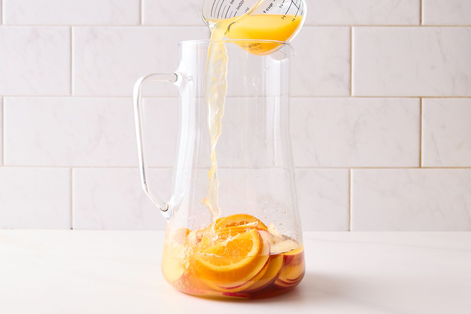A pitcher containing sliced fruit is being filled with a liquid
