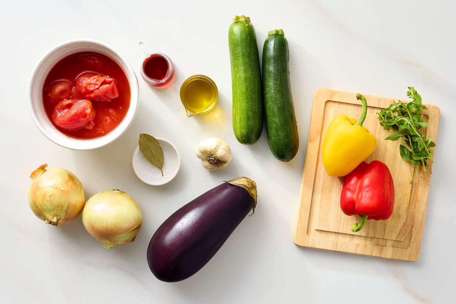 Ingredients for making ratatouille including tomatoes onions eggplant zucchini bell peppers garlic oil and seasonings
