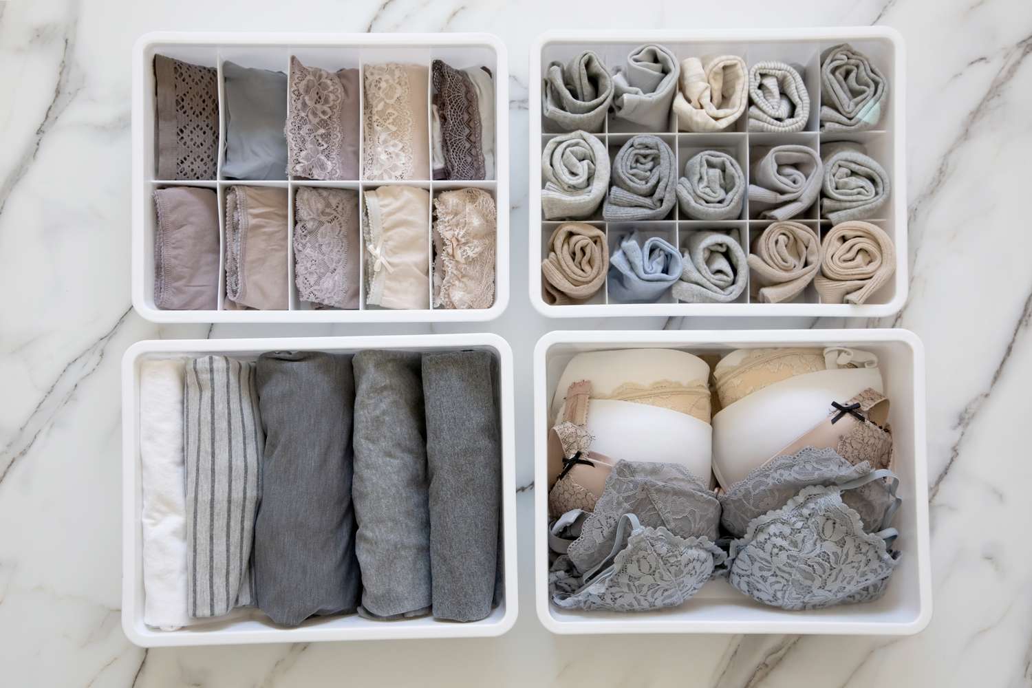 Womans underwear, pajamas and socks neatly folded and placed in closet organizer drawer divider on white marble table. Declutter wardrobe of undergarments. Keeping organized lingerie drawer storage.