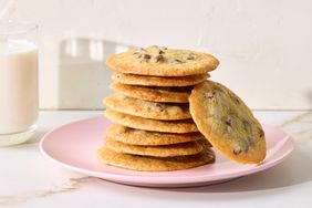 A stack of chocolate chip cookies on a pink plate a glass of milk nearby