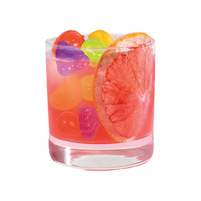 A glass filled with gummy candies and a slice of citrus fruit on the rim