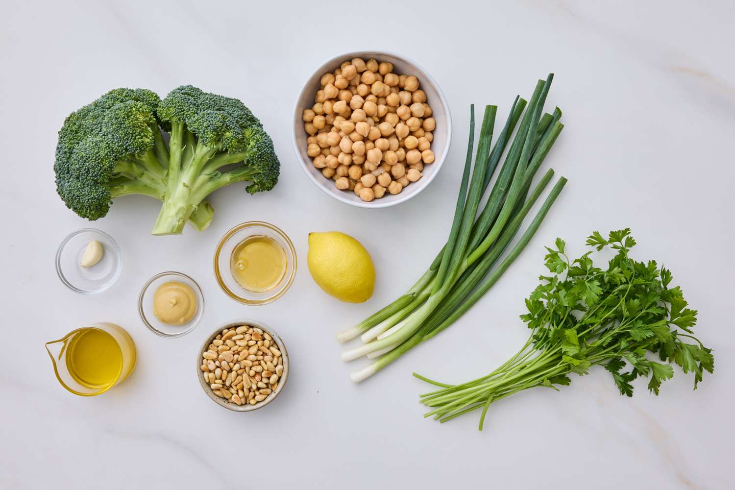 Ingredients for a broccoli and chickpea salad including broccoli chickpeas green onions a lemon parsley pine nuts and dressings