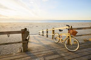 A bike with a basket parked on a wooden boardwalk leading to a beach
