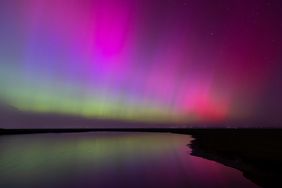 Aurora borealis with vivid colors reflected over a calm water surface and silhouetted horizon