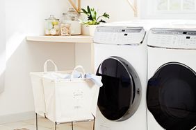 A laundry room setup featuring a washer and dryer beside a cart with laundry bags with shelves and decorations in the background