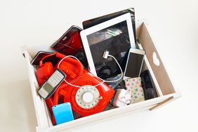 A box containing assorted electronic and phone devices including retro and modern styles