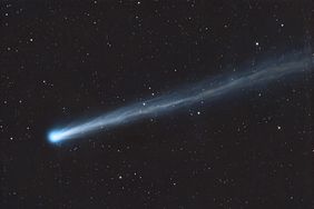 A comet streaking across a starfilled night sky showing a bright nucleus and a long tail extending to the right
