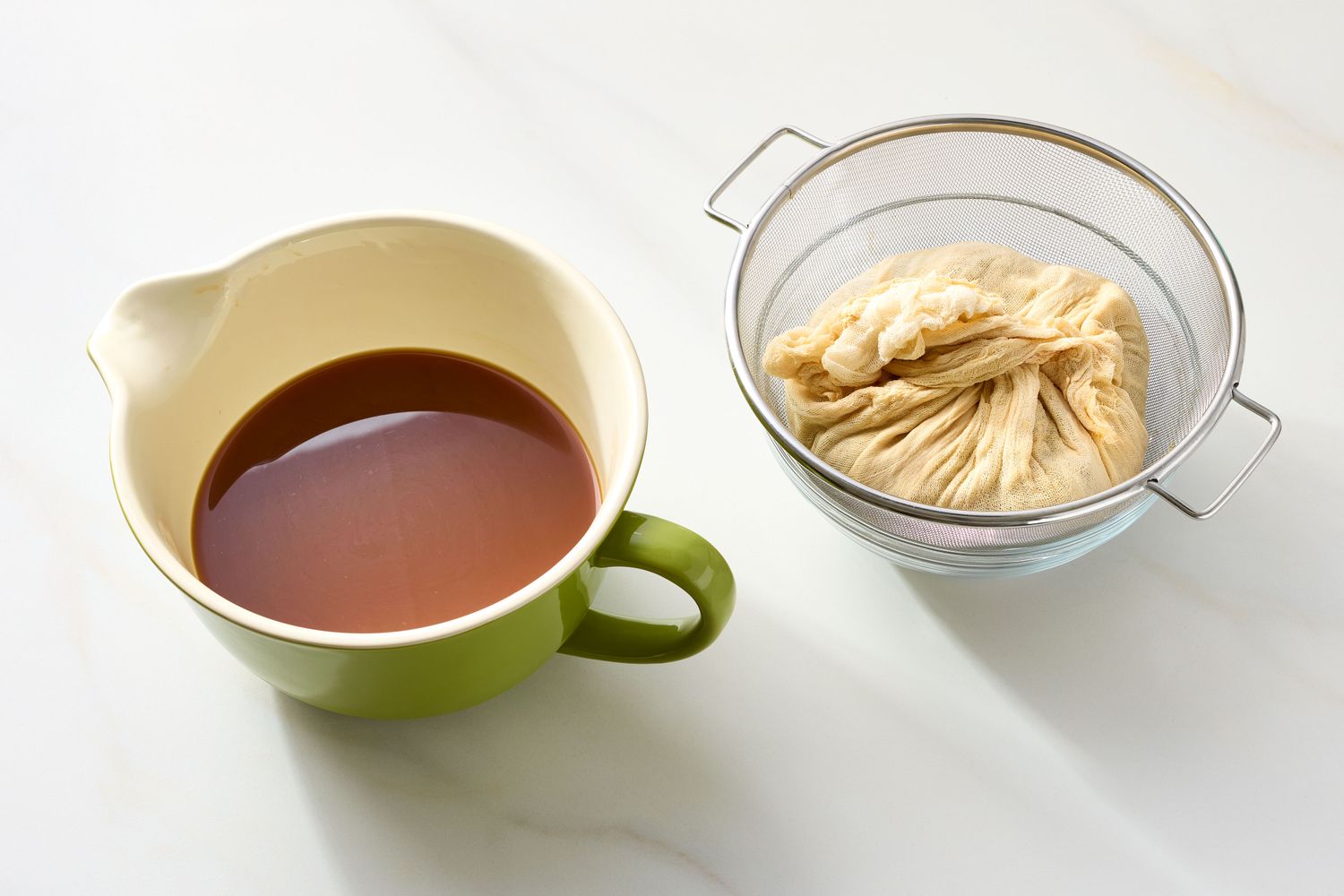 A bowl of apple cider alongside a strainer containing pulp wrapped in cheesecloth