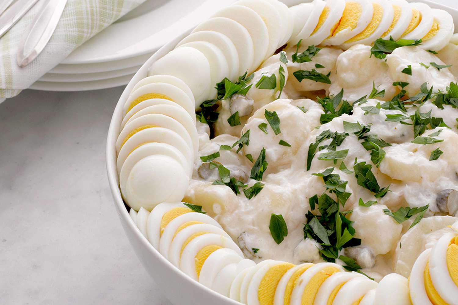 Potato salad garnished with parsley and sliced boiled eggs in a white bowl