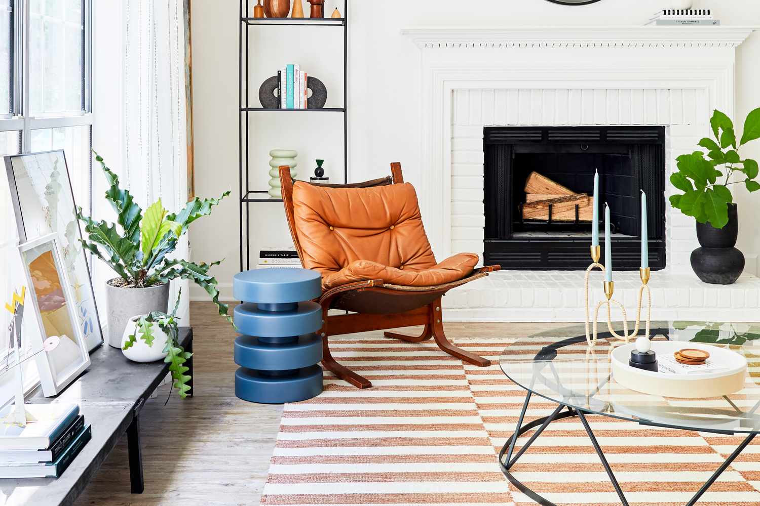 A cozy living room with a leather chair a striped rug a fireplace and houseplants