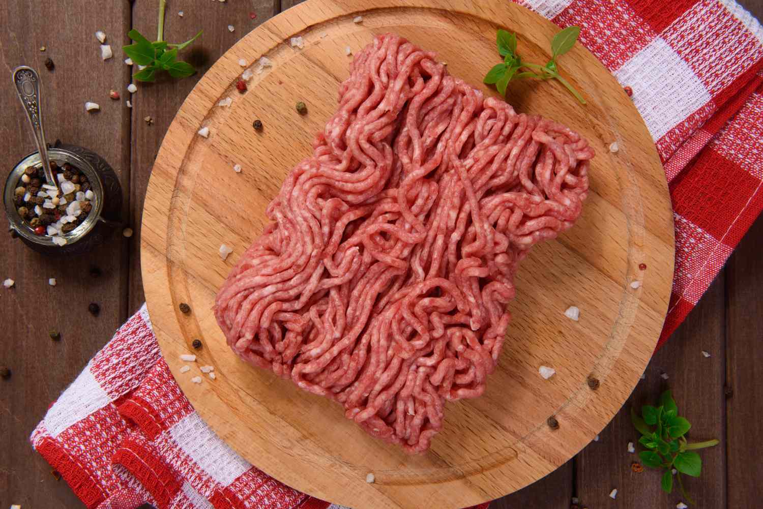 Raw ground meat on a wooden cutting board with a red-checkered cloth underneath