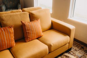 A mustardcolored sofa with two striped accent pillows in a room by a window