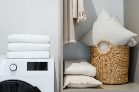 Laundry corner with folded towels a washing machine and a woven basket with pillows