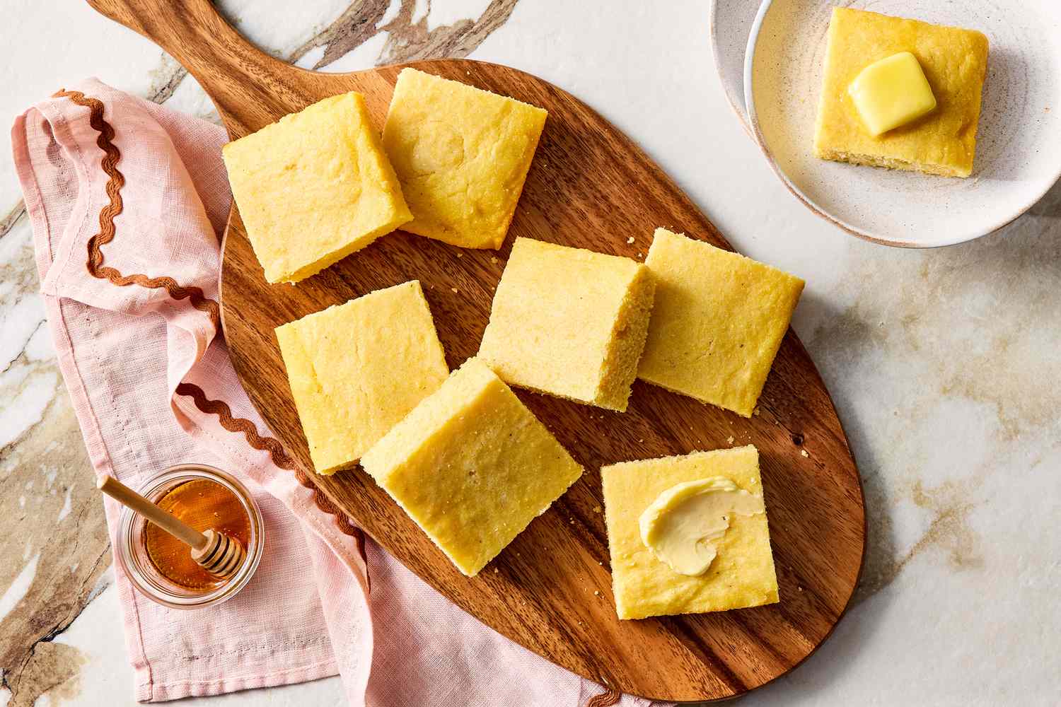 Slices of cornbread on a wooden board with butter and honey