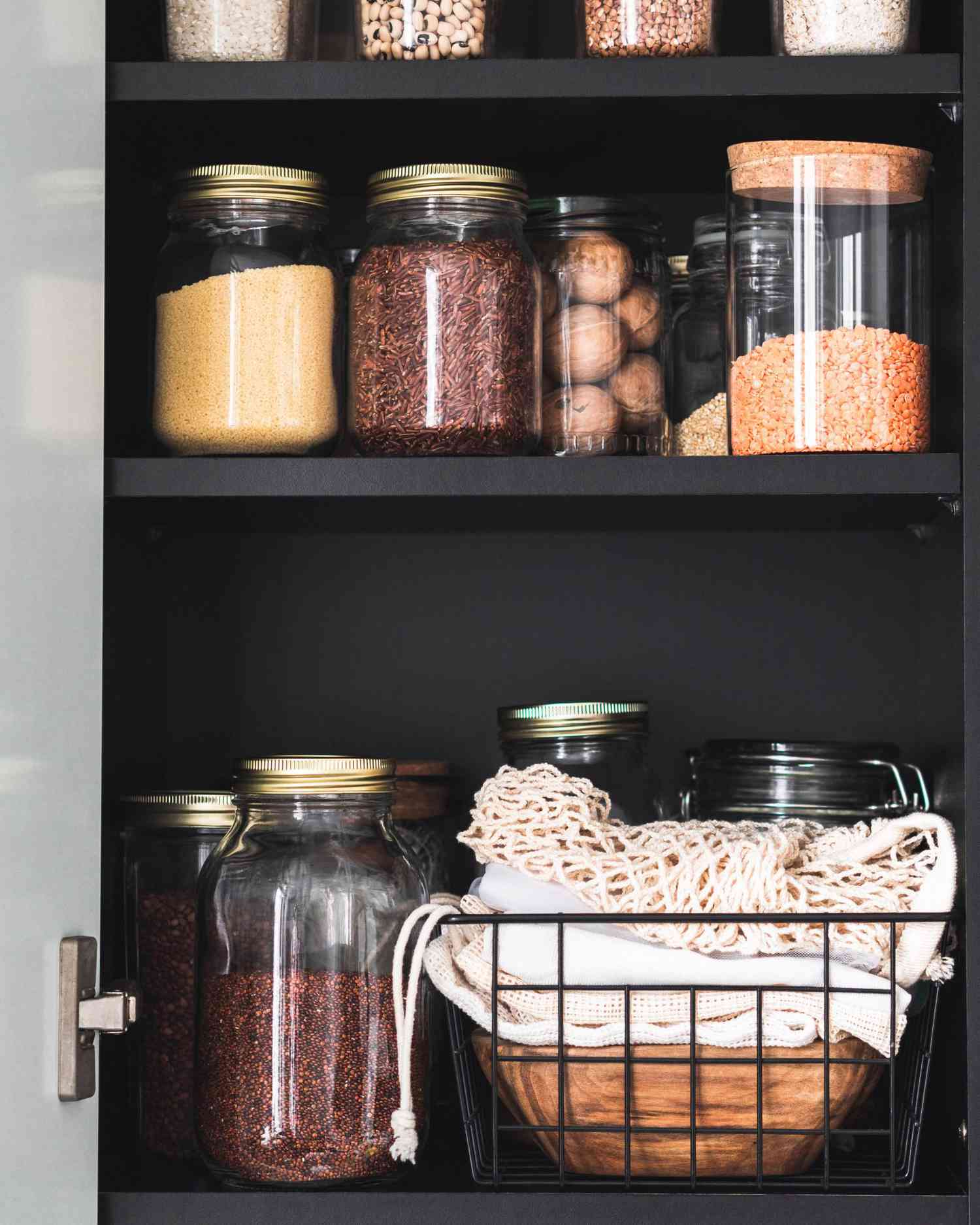 Black shelf in the kitchen with various cereals and seeds in glass jars.