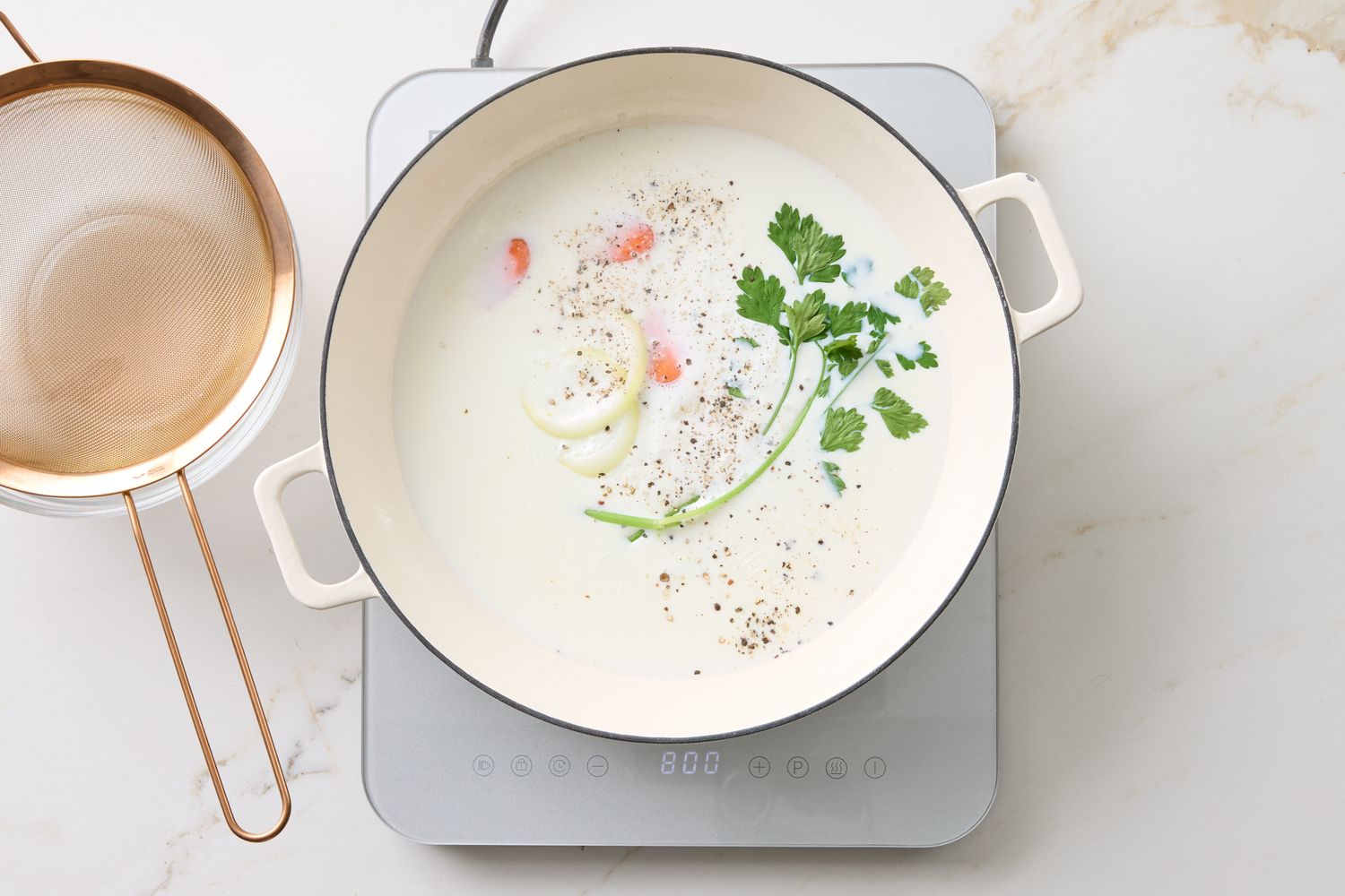 Ingredients cooking in a pot on a countertop including milk seasoning and fresh herbs