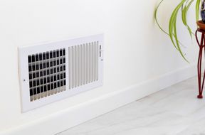 A wallmounted air vent with visible slats and a nearby green plant