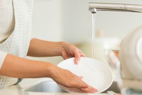 Person rinsing a plate under running water in a sink