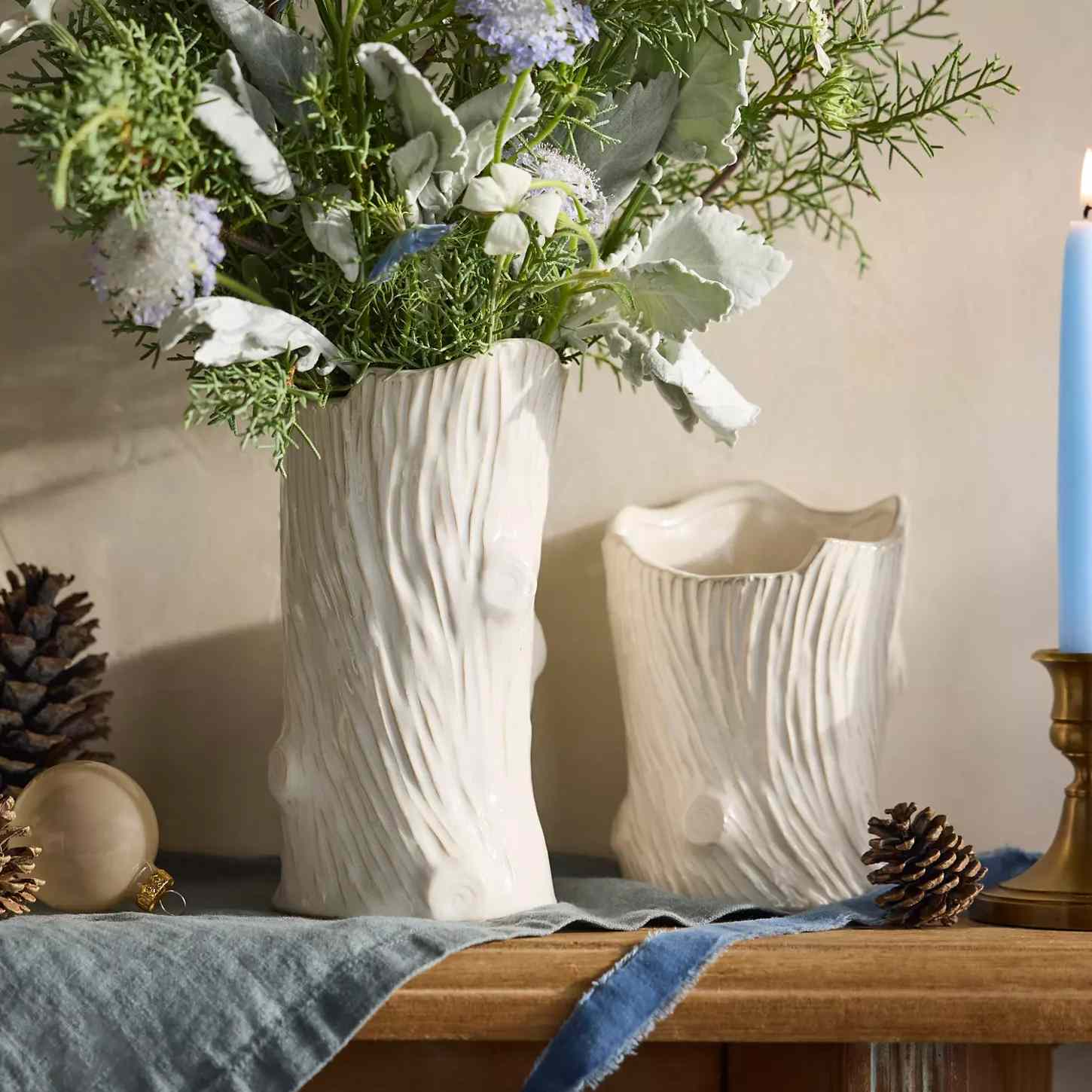 Two white vases designed to resemble tree trunks one holding a floral arrangement displayed on a wooden surface with decorative elements