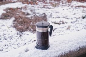 A French press coffee maker placed on a snowy surface outdoors