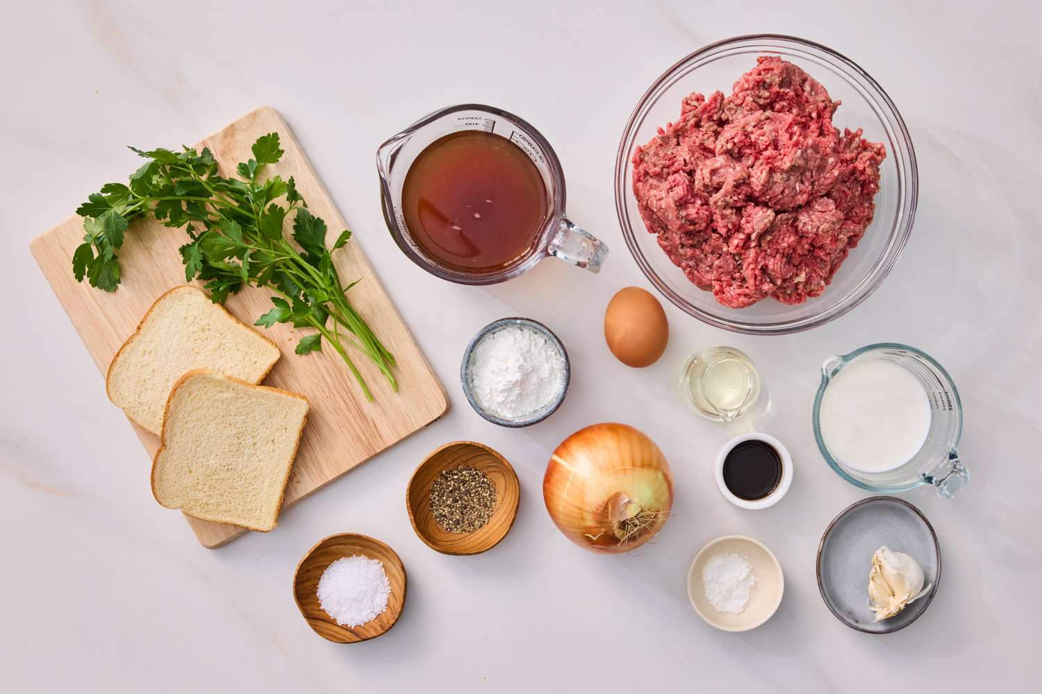 Ingredients for Salisbury steak and onion gravy on a countertop including ground beef bread broth onions and spices