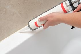 Hands applying caulk to the edge of a bathtub using a caulking gun