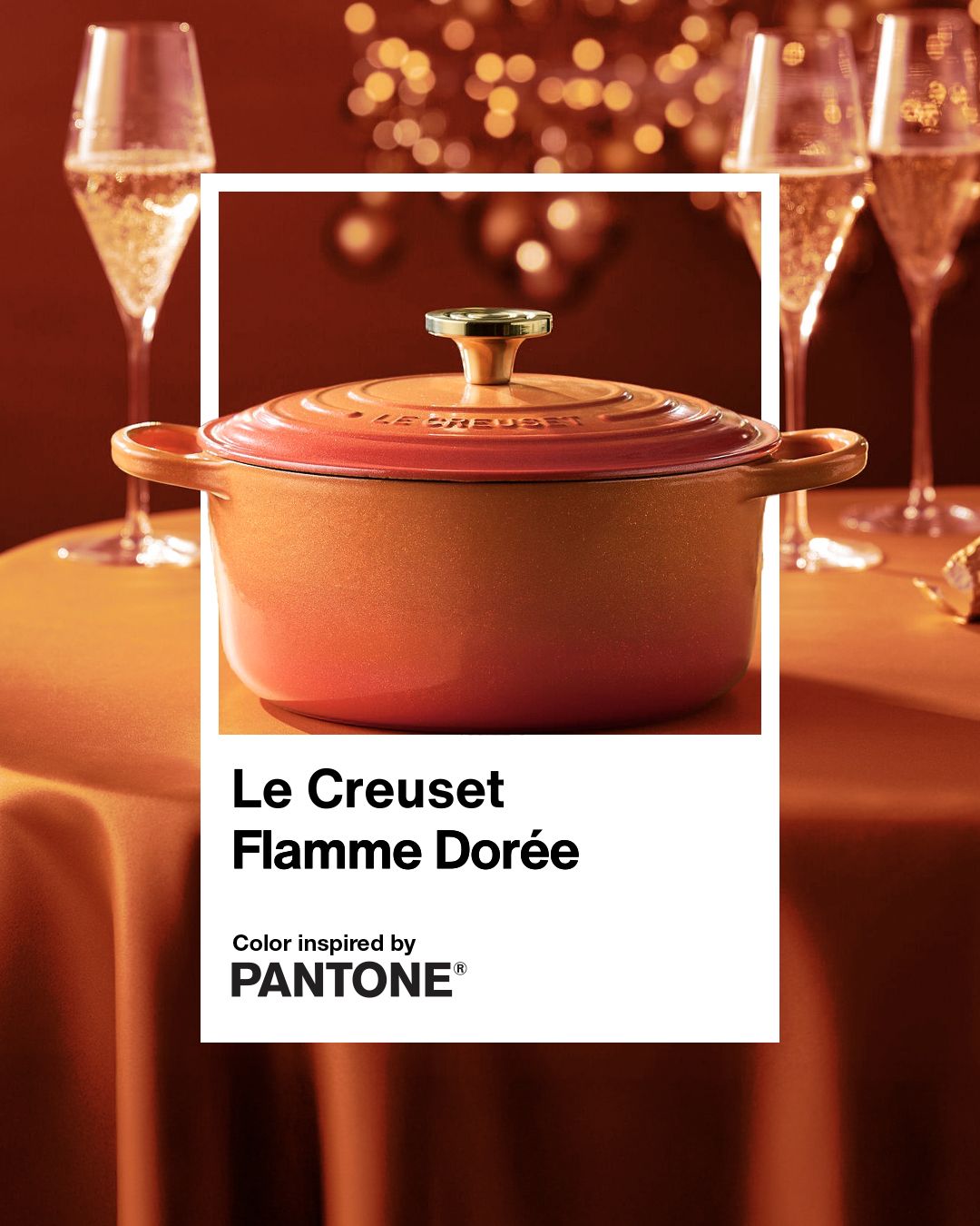A Le Creuset Flamme Dore pot displayed on a table accompanied by champagne glasses and lighting decorations in the background highlighted with Pantone branding