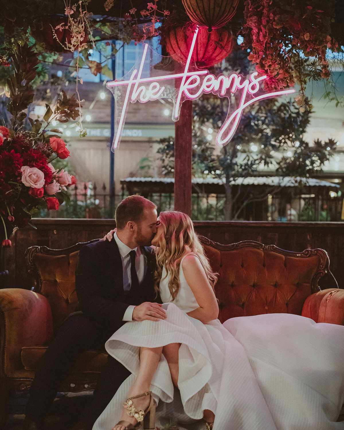 wedding after party bride and groom kissing on couch beneath neon sign