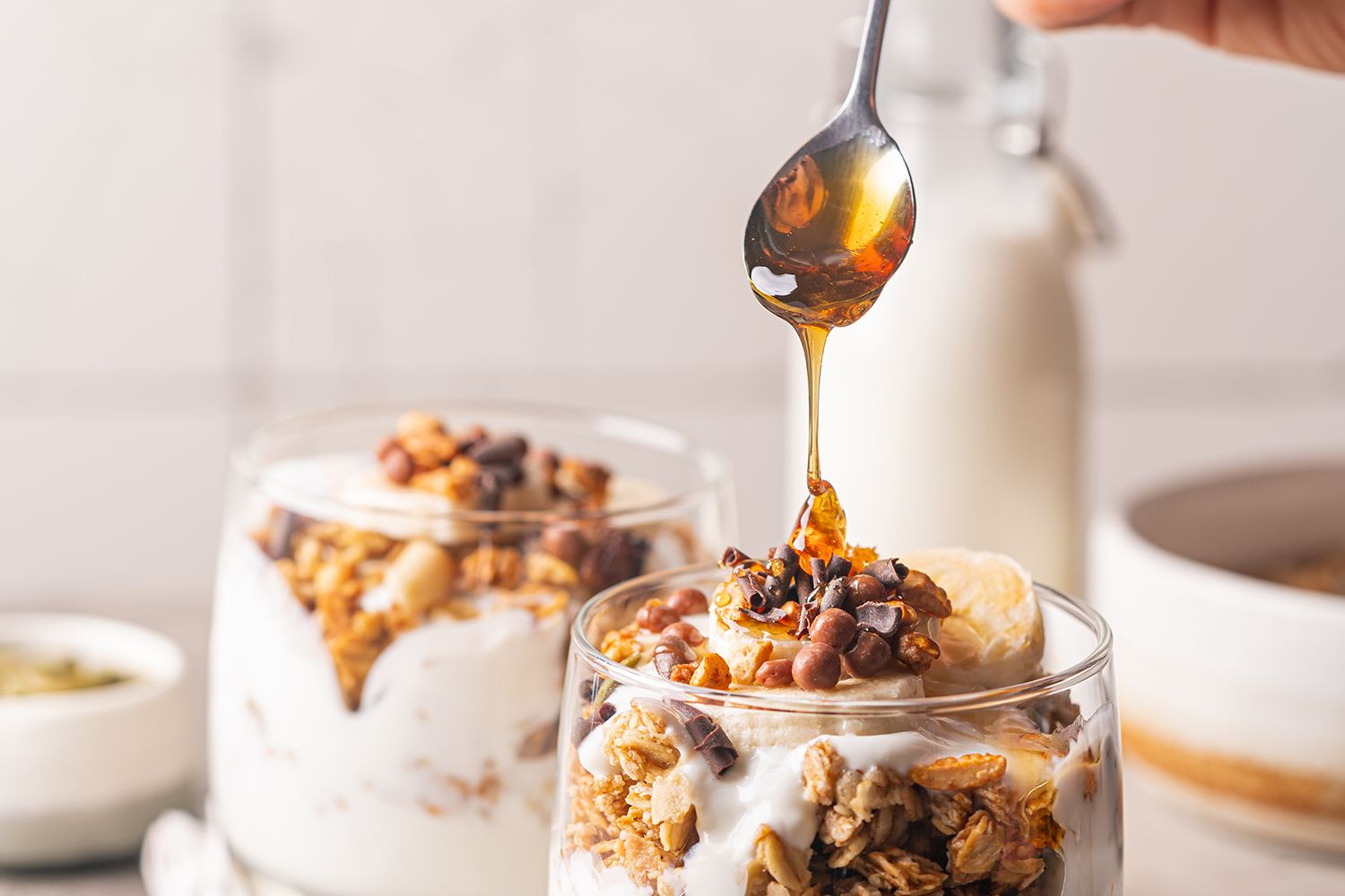 Granola and yogurt in glasses with a spoon drizzling honey in the foreground