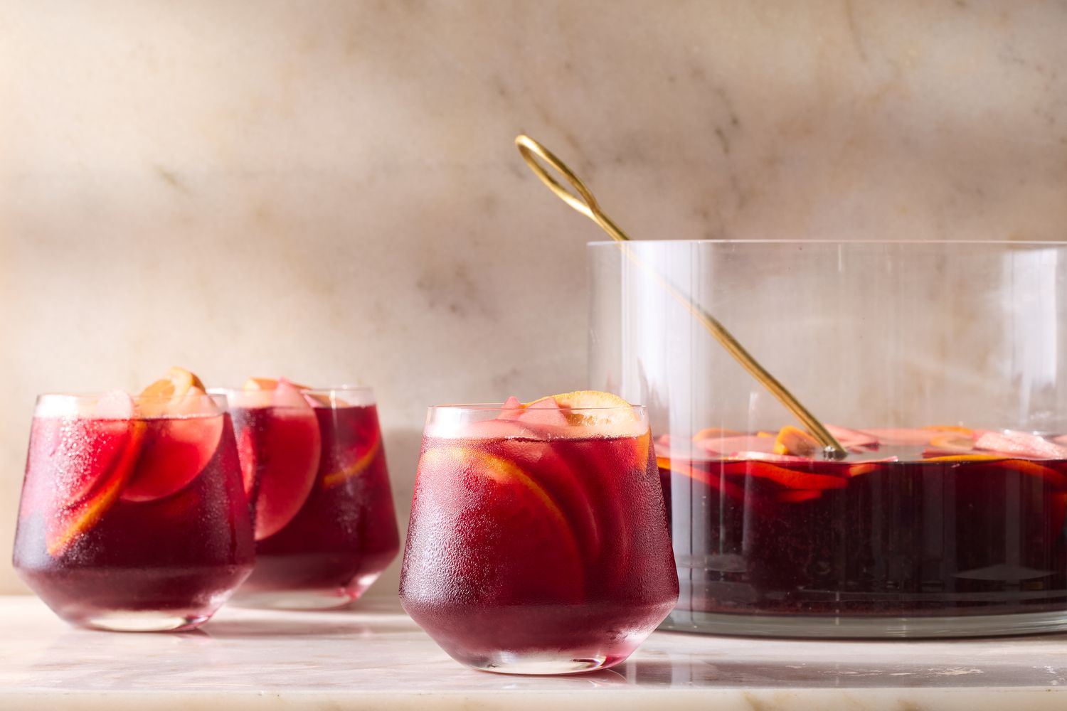 A serving of red sangria in glasses and a punch bowl with a golden ladle