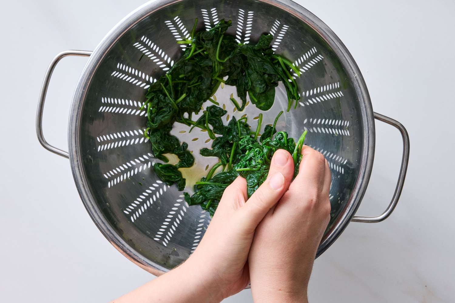 Hands squeezing cooked spinach over a colander