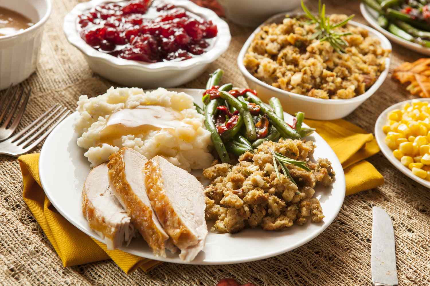 Plate with turkey mashed potatoes stuffing green beans cranberries and corn with additional bowls in the background