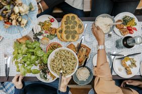 Top view of a group dining together at a dinner party, sharing various dishes and a bowl of pesto pasta