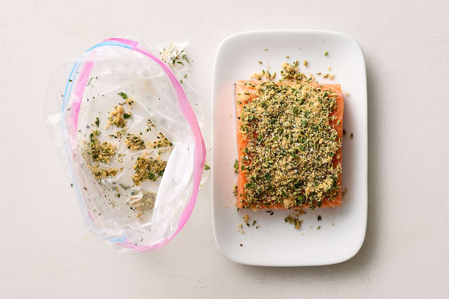Uncooked salmon covered with seasoning on a white plate plastic bag with leftover seasoning mix to the side