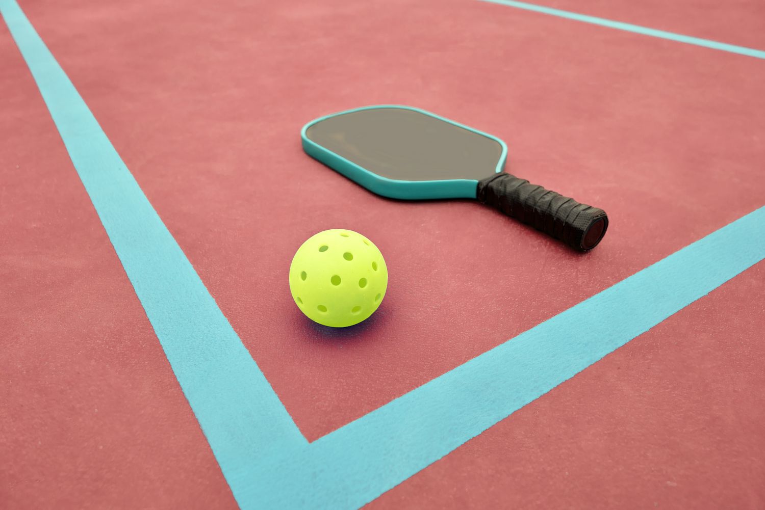 Pickleball paddle and ball resting on a court surface
