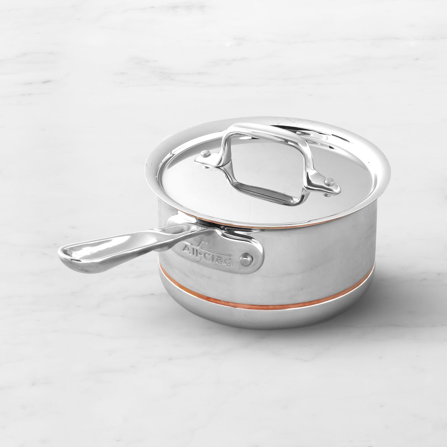 A stainless steel saucepan with a lid and a metal handle placed on a smooth surface