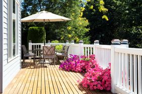 A wooden deck with patio furniture umbrella and pink flowers along the railing