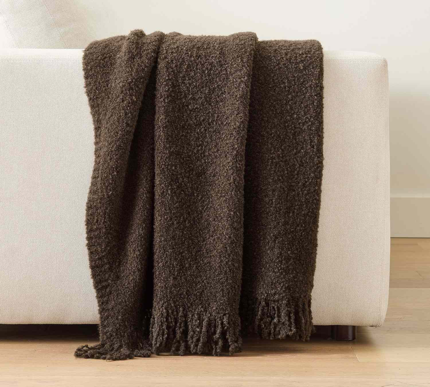 A boucle knit throw draped over the back of a white sofa featuring a cozy texture and fringed edge