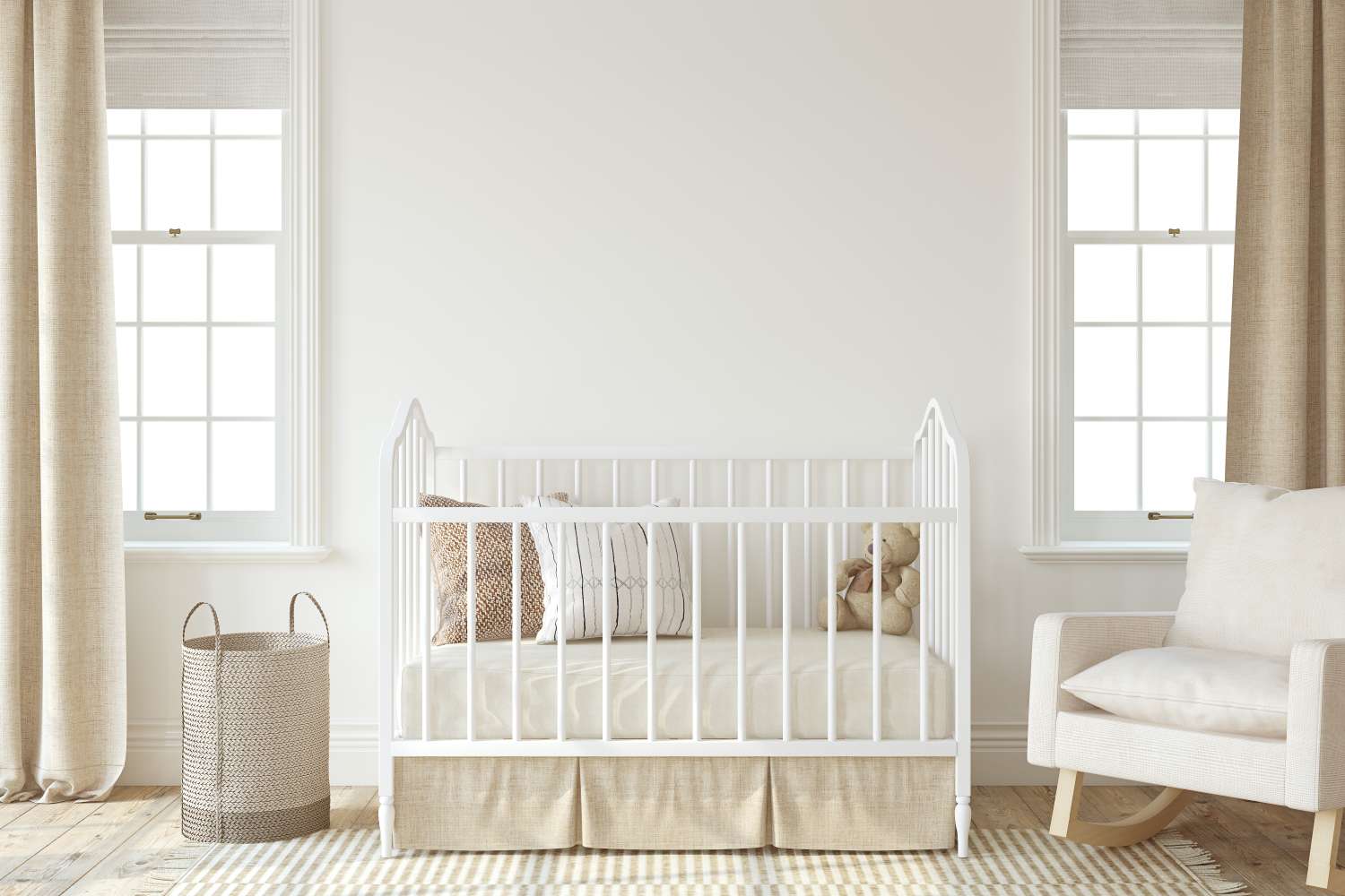 A nursery with a crib an armchair and a basket positioned beneath two windows with curtains