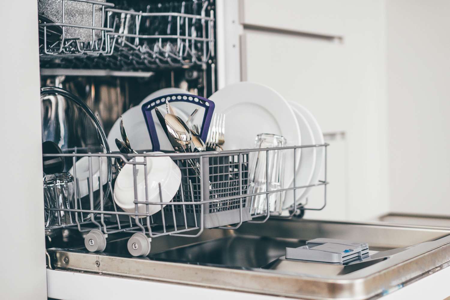 Open dishwasher with the lower rack loaded with dishes and cutlery