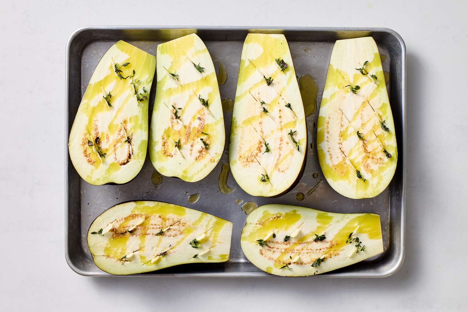 Halved eggplants seasoned with oil and herbs on a baking tray prepared for baking