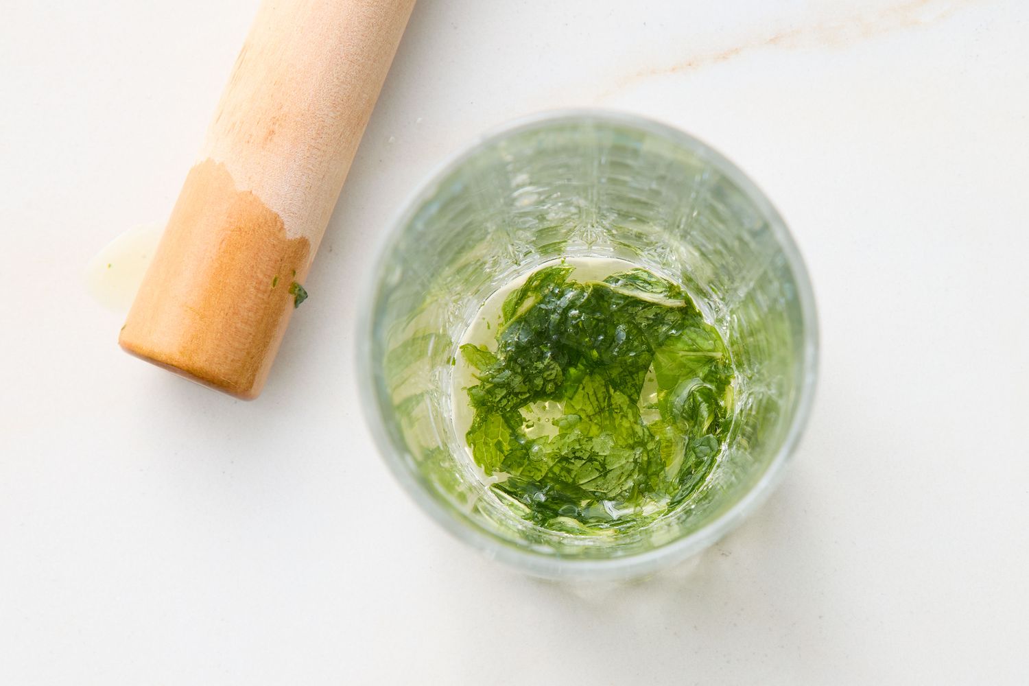 Muddled mint leaves in a glass with a wooden muddler nearby