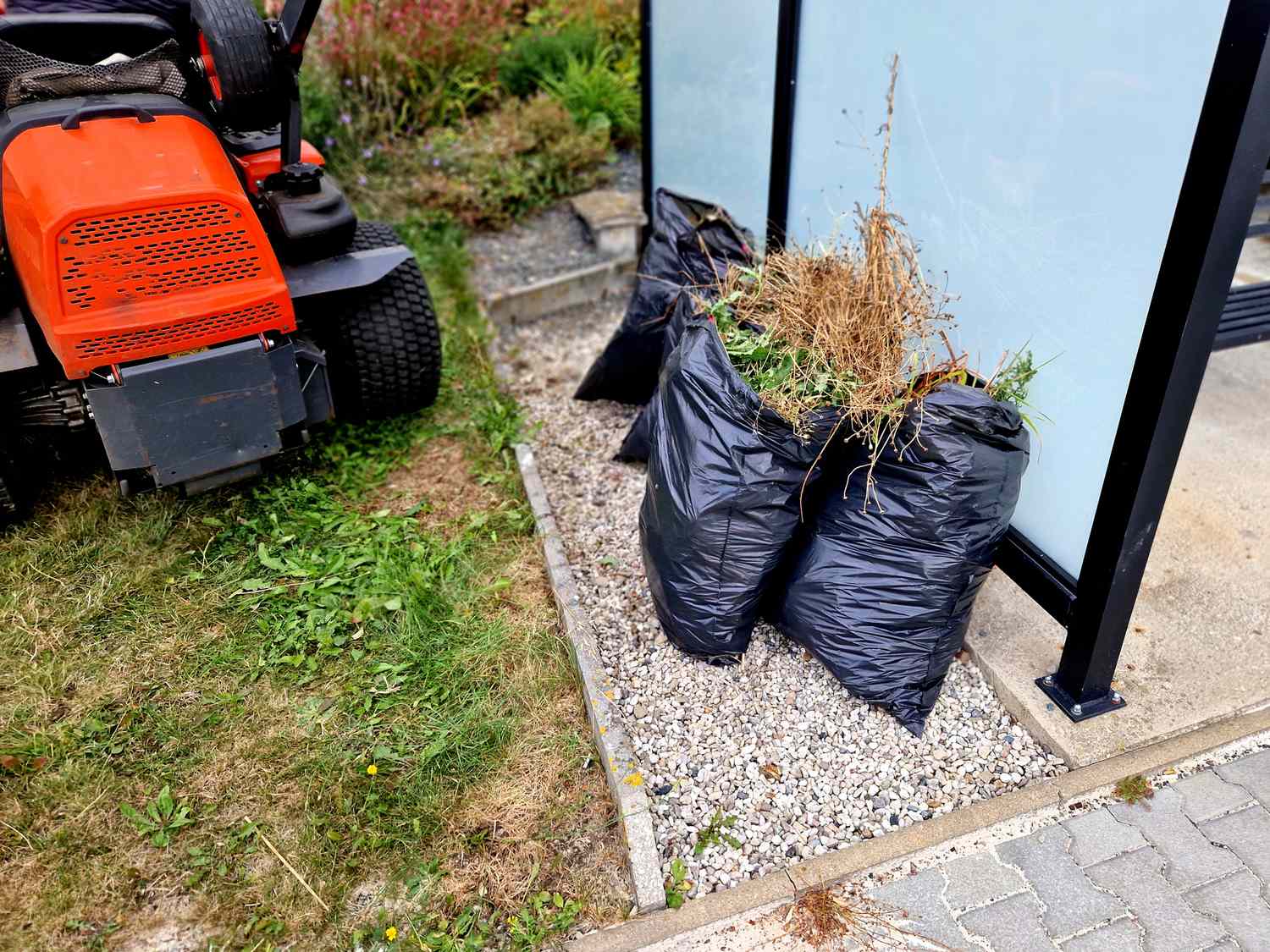 Bags filled with garden waste next to a riding lawn mower near a patio