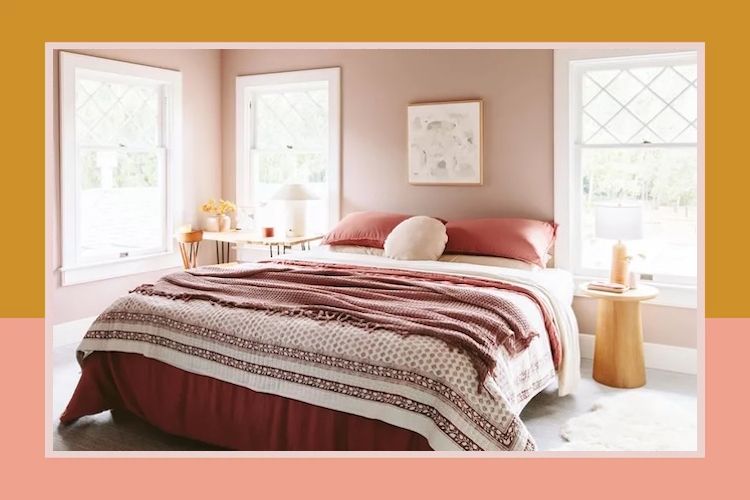 A bedroom with a bed featuring layered textiles surrounded by windows and side tables